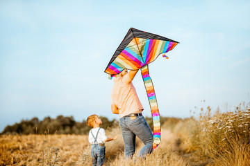 Father and son walking together with colorful air kite on the field, back view. Concept of a happy family during the summer activity