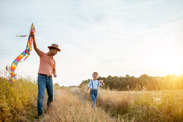 Father and son walking together with colorful air kite on the field during the sunset. Concept of a happy family