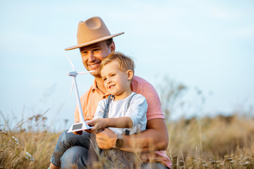 Father with young son playing with toy wind turbine in the field. Concept of knowledge of the green...