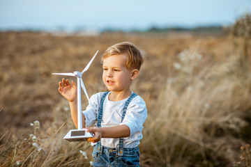 Curious young boy playing with toy wind turbine in the field, studying how green energy works from...
