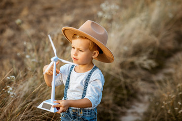 Curious young boy playing with toy wind turbine in the field, studying how green energy works from...