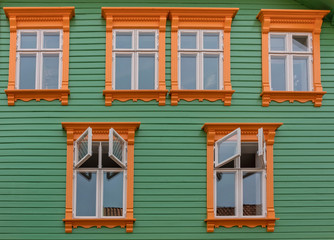Fototapeta premium Orange windows on the green wall of green wooden house, Stavanger, Norway