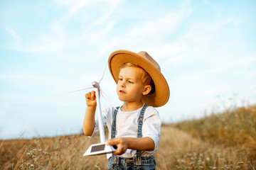 Portrait of a curious young boy playing with toy wind turbine in the field, studying how green...
