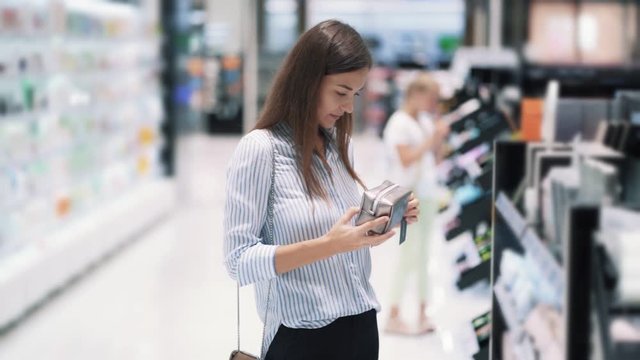 Beautiful young woman chooses makeup bag in cosmetics shop, slow motion