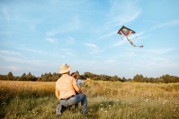 Father with son launching colorful air kite on the field during the sunset. Concept of a happy family having fun during the summer activity