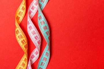 Top view of spiral colorful measure tapes on red background. Concept of perfect female figure with...
