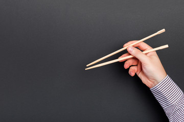 Male hand with chopsticks on black background. Traditional asian food with emty space for your design