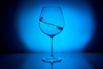 Water glass with splash on blue lighting reflection background