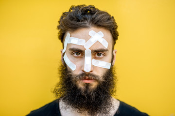 Close-up portrait of an injured man with medical patches on his face on the yellow baackground