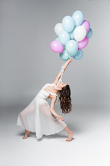 Fototapeta na wymiar graceful ballerina in white dress dancing with festive balloons on grey background