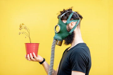 Portrait of a sad man with gas mask and dried flowerpot on the yellow background. Concept of poor...