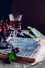 One glass with cherry liquor and cherry berries on an old book. Still life