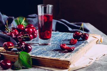 A wineglass with cordial and cherry berries on an old book. Still life