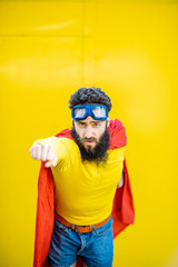 Fototapeta premium Portrait of a man like a superhero in colorful clothes and pilot's glasses on the yellow background