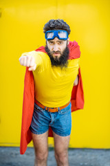 Portrait of a man like a superhero in colorful clothes and pilot's glasses on the yellow background