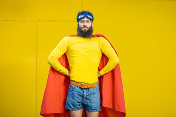 Portrait of a man like a superhero in colorful clothes and pilot's glasses on the yellow background