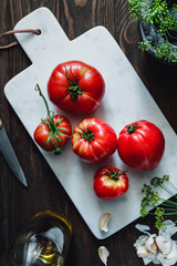 Top view of brandywine sort tomatoes with ingredients for seasonal canning on a white marble tray.