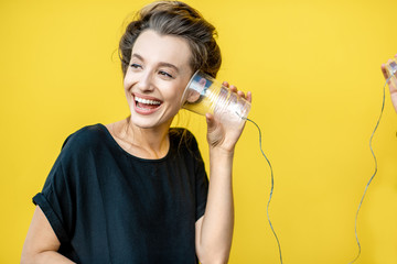Happy woman listening to a cup, using string phone on a yellow background. Concept of communication...