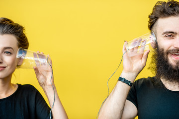 Man and woman talking with string phone made of cups on the yellow background. Concept of communication - obrazy, fototapety, plakaty