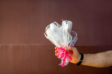 Man holding a bouquet made of plastic garbage on the dark red background. Concept of non-recyclable plastic pollution