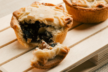 Two mince pies on the wooden surface with broken off piece