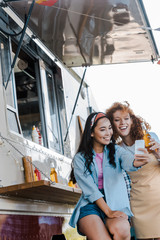 selective focus of cheerful multicultural girls taking selfie near food truck