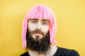 Close-up portrait of a stylish man with beard and long color hair on the yellow background