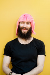 Funny portrait of a stylish playful man with beard and long color hair with expressive emotions on the yellow background