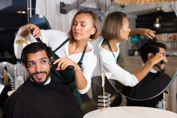 woman hairdresser shaving hair of smiling man