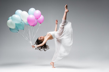 graceful ballerina in white dress dancing with festive balloons on grey background