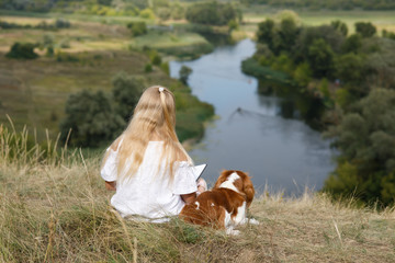 Young girl in the white dress reads the book  with her dog outdoors