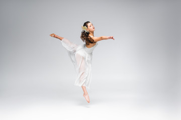 young graceful ballerina dancing in white dress on grey background