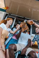 low angle view of happy multicultural friends clinking bottles with beer near food truck