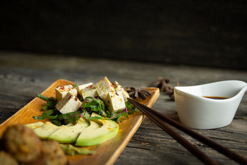 Tofu in Nahaufnahme mit Stäbchen, Gemüse, Obst und Gewürzen und Schüssel Sojasauce