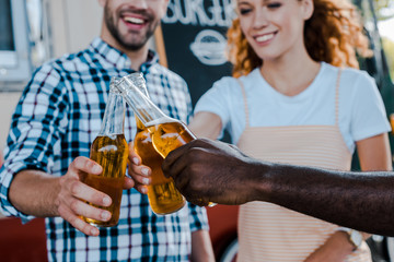 cropped view of happy multicultural men clinking with redhead woman near food truck