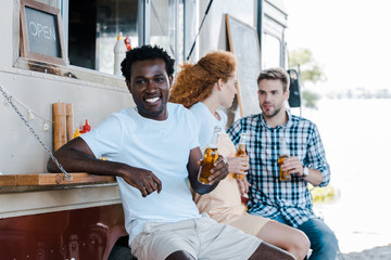 selective focus of cheerful african american man holding bottle of beer near friends