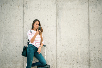 Woman using smart phone while leaning on the luggage on the street.