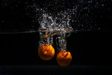 Ripe fruit tangerines fall into the water. Drops, a splash of water on a black background. Slow...