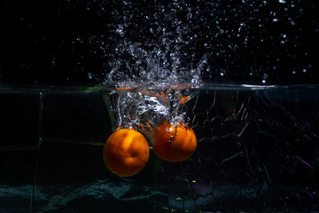 Ripe fruit tangerines fall into the water. Drops, a splash of water on a black background. Slow...