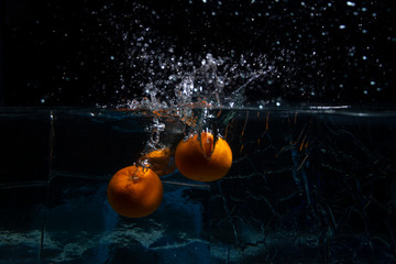 Ripe fruit tangerines fall into the water. Drops, a splash of water on a black background. Slow...