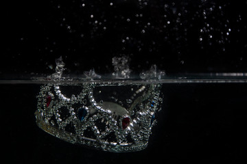 The silver crown falls into the water. A splash of water, drops on a black background. © Romafa