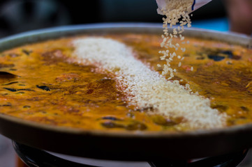 Seafood paella in its paella pan while rice falls.