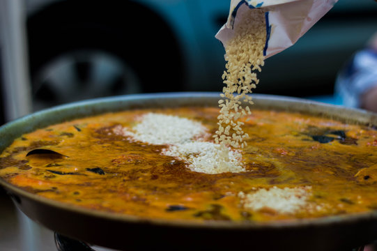 Seafood paella in its paella pan while rice falls.