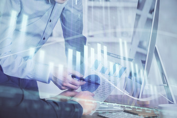 Double exposure of chart with businessman typing on computer in office on background. Concept of...