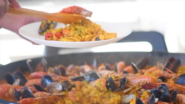 Paella traditional Spanish food. Person putts seafood paella from the fry pan to plate. Paella with with mussels, king prawns, langoustine and squids. Slow motion 4K UHD video footage. 3840X2160