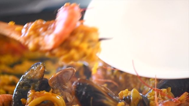 Paella traditional Spanish food. Person putts seafood paella from the fry pan to plate. Paella with with mussels, king prawns, langoustine and squids. Slow motion 4K UHD video footage. 3840X2160