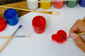 Skilled female painter creating image of heart with paintbrush and gouache on paper 