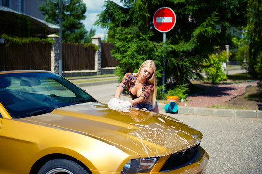 Young blond sexy model girl washing golden luxury car with foam outdoors