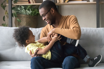 Happy African American father playing with toddler son at home