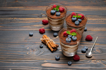 Classic tiramisu dessert with blueberries and strawberries in a glass cup on wooden background